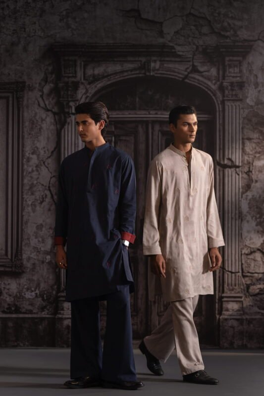 Navy panjabi with red cuffs beside an ivory embroidered set