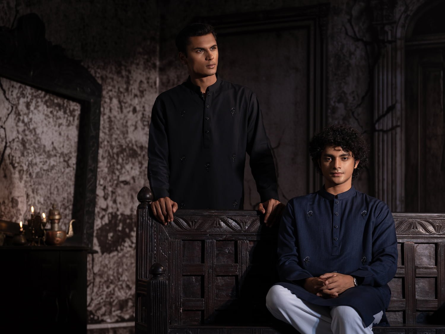 Two models in black and navy embroidered panjabis beside a carved wooden bench